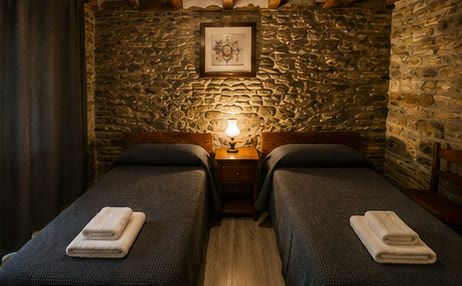 Habitació amb dos llits individuals i paret de pedra