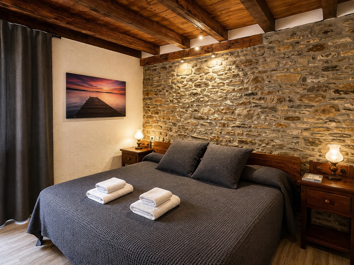 Habitació doble de l'Hostal Rusó amb paret de pedra vista i sostre de bigues de fusta